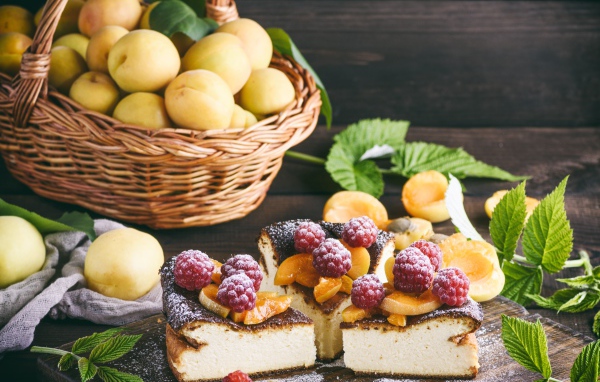 Вкусный фруктово - ягодный пирог на столе с корзиной с абрикосами