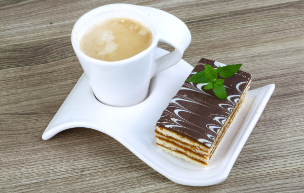 Чашка капучино на тарелке с пирожным 