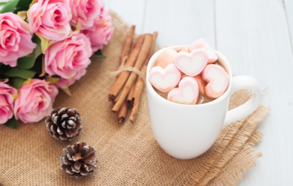 Чашка какао с маршмеллоу на столе с корицей, шишками и букетом розовых роз