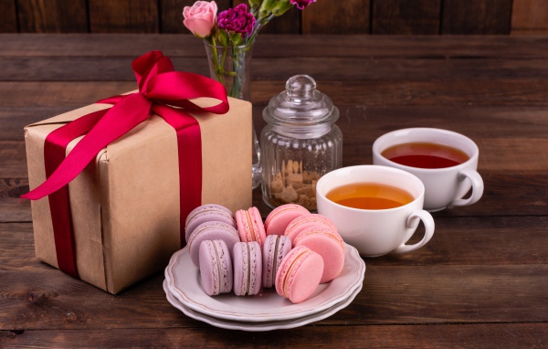 Подарок с красной лентой на столе с макарунами и чаем 