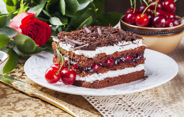 Кусок торта с вишней, шоколадной крошкой на столе с розой