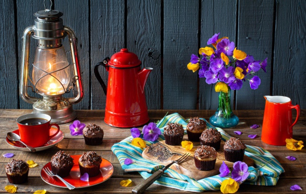 Аппетитные свежие кексы с кремом на столе с кофе, лампой и букетом цветов