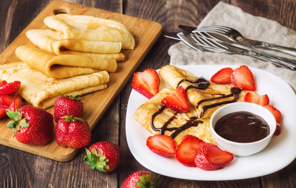 Аппетитные тонкие блинчики на столе с шоколадом и свежей клубникой