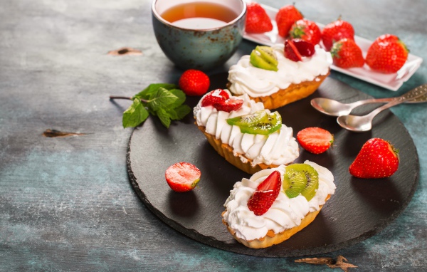 Пирожные с киви и клубникой на столе с чаем