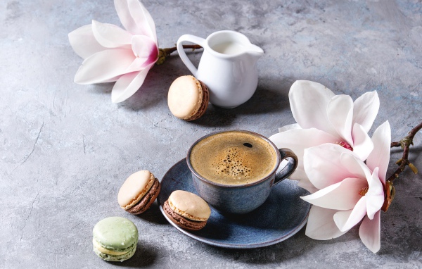 Кофе на столе с макарунами, молоком и цветами 