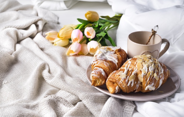 Круассаны на кровати с кофе и букетом тюльпанов