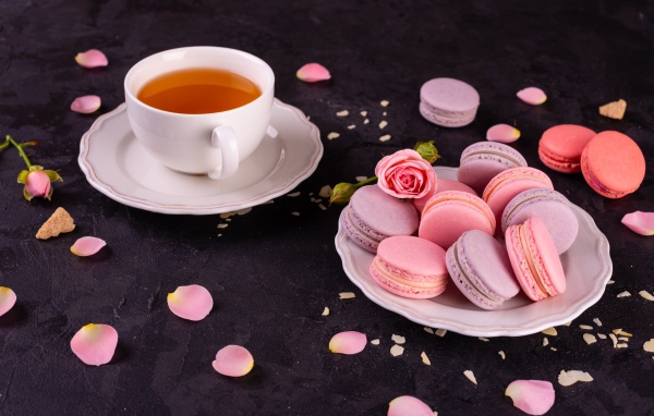 Нежный десерт макарон на столе с чашкой чая и розой