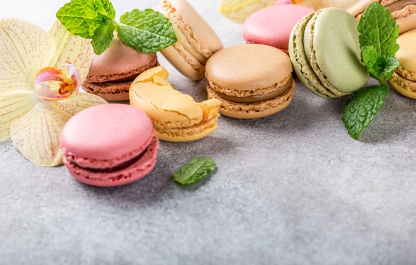 Десерт макарон на серой поверхности с цветами орхидеи и мятой