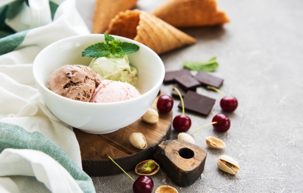 Шарики мороженого на столе вафельными рожками, черешней и фисташками