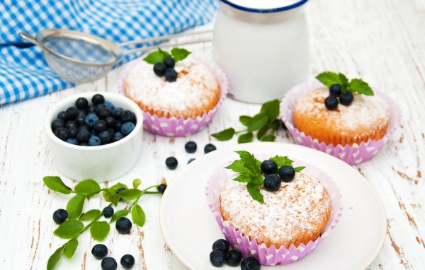 Кексы с сахарной пудрой на столе с молоком и черникой