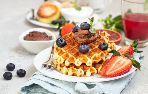 Сладкая вафля с шоколадом, ягодами черники и клубники на тарелке