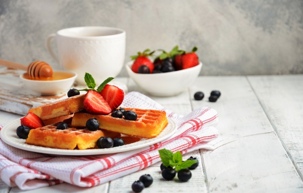 Сладкие вафли с ягодами черники и клубники на столе с медом и чаем