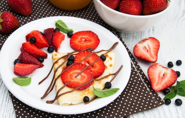 Тонкий блинчик на тарелке с шоколадом, ягодами клубники и черники