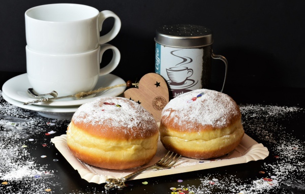 Два пончика с сахарной пудрой на черном фоне с белыми чашками