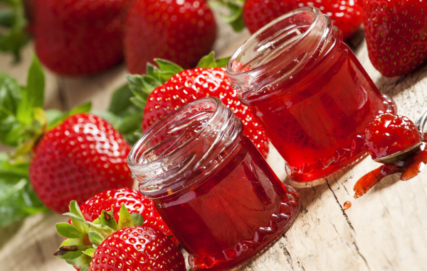 Две баночки клубничного джема на столе с клубникой