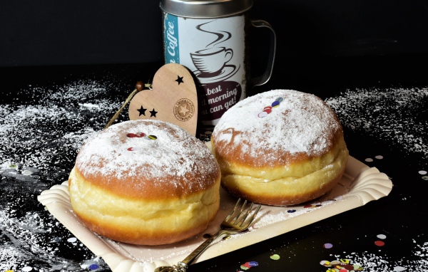 Два пышных пончика с сахарной пудрой на черном столе с кофе