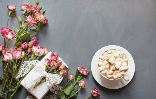 Чашка кофе с маршмеллоу на столе с подарком и букетом роз