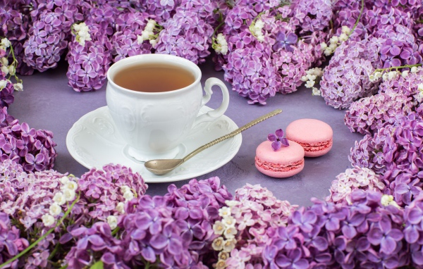 Чашка чая на столе с цветами сирени и десертом макарон