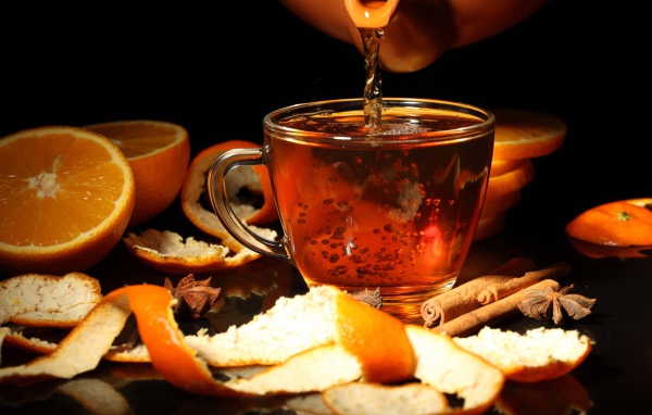 Стеклянная чашка с чаем на столе с апельсинами и корицей
