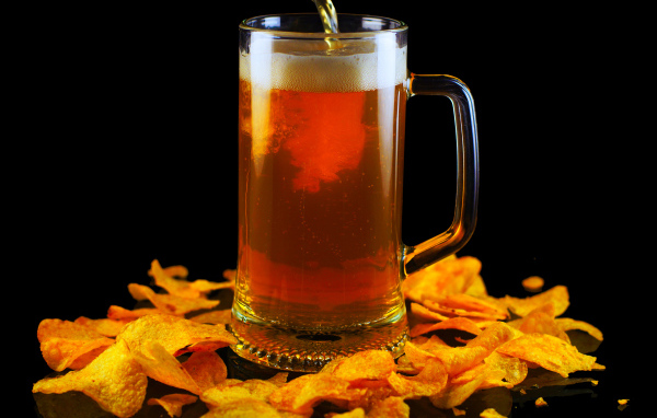 Бокал пива с чипсами на черном фоне