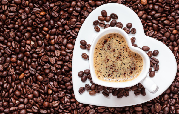 Белая чашка в форме сердца стоит на кофейных зернах 