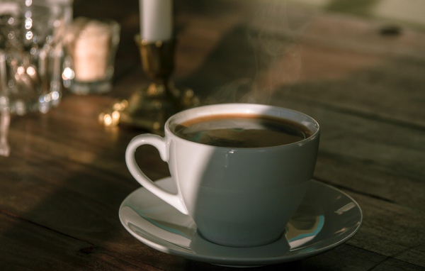 Белая чашка кофе на столе в лучах солнца