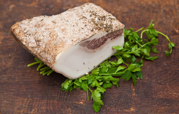 Кусок сала со специями на столе с зеленью петрушки