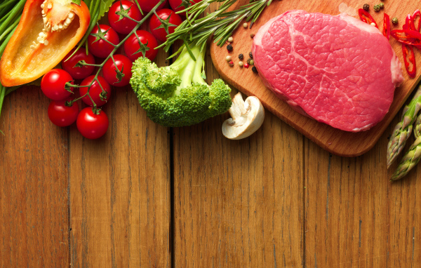 Кусок свежего мяса на столе с овощами и зеленью 