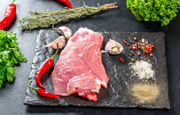 Кусок мяса на столе с острым перцем, чесноком и зеленью
