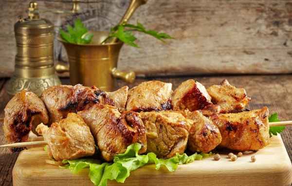 Аппетитный шашлык лежит на разделочной доске с листьями салата