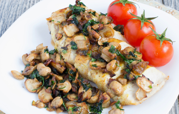 Аппетитный кусок куриного филе с грибами на тарелке с помидорами 