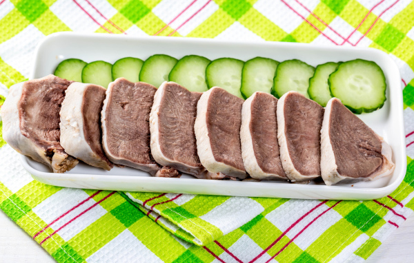 Вареный язык на тарелке со свежими огурцами