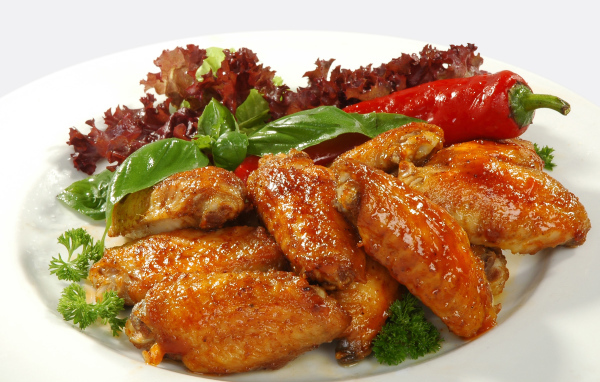 Жареные куриные крылышки на тарелке с острым перцем и зеленью 