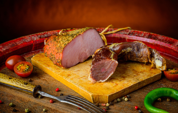 Ветчина и вяленое мясо на разделочной доске на столе с помидорами и горьким перцем 