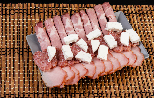 Колбаса и ветчина на тарелке с кусочками сыра фета