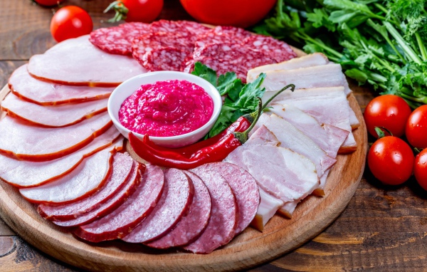 Мясная нарезка на доске с соусом, красным перцем,  помидорами и зеленью 