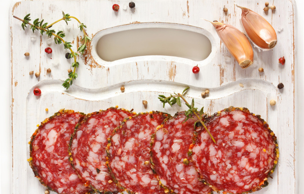 Нарезанная колбаса на разделочной доске со специями и чесноком