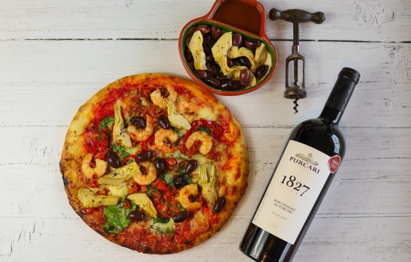 Пицца на столе с оливками и бутылкой вина