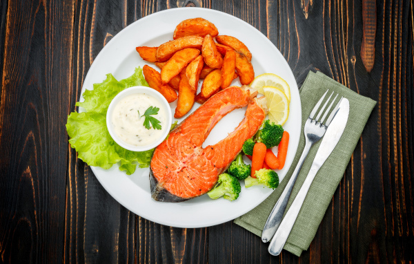 Кусок красной рыбы на тарелке с картофелем и соусом