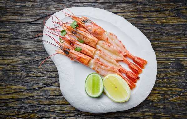 Аппетитные креветки на белой тарелке с лимоном