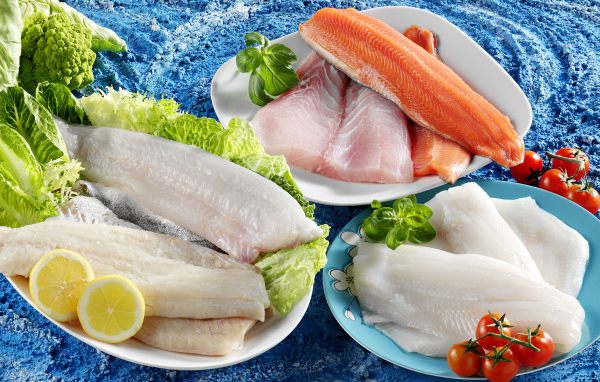 Филе рыбы на тарелках с помидорами и листьями салата