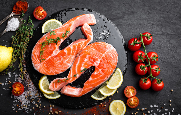 Два куска красной рыбы с овощами на черном фоне