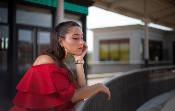 Задуманная девушка в красном платье стоит у перил 