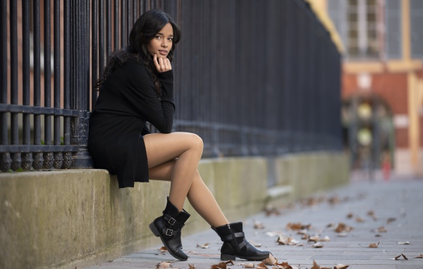 Молодая девушка в черном сидит у железного забора