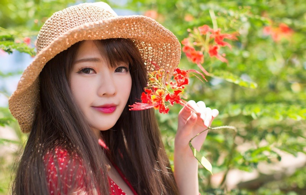 Девушка азиатка в шляпе с красным цветком