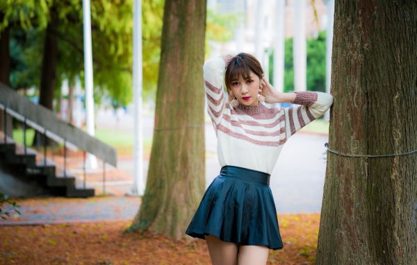 Девушка азиатка стоит в короткой юбке у дерева