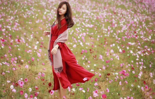Красивая азиатка в красном платье на поле с цветами космеи