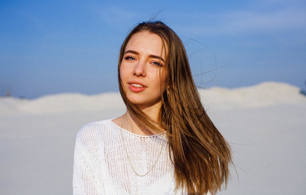 Красивая голубоглазая девушка в белом свитере на фоне голубого неба