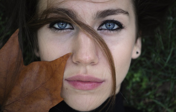 Красивая голубоглазая девушка с желтым листом у лица