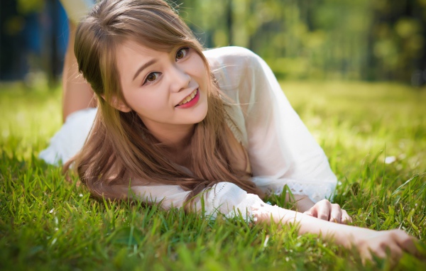 Красивая кареглазая девушка азиатка лежит на зеленой траве